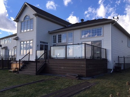 dark custom deck attached to two storey home with glass railings