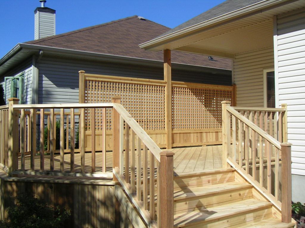 Wooden custom deck attached to bungalow with stairs leading to backyard