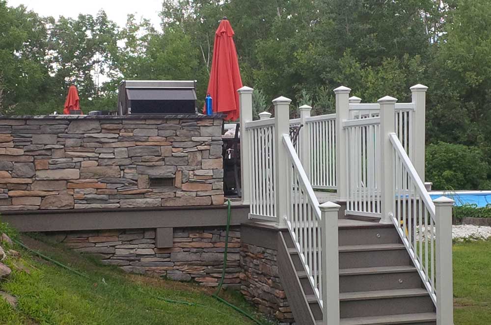 custom deck with stone walls and stairs with railings leading to backyard grass