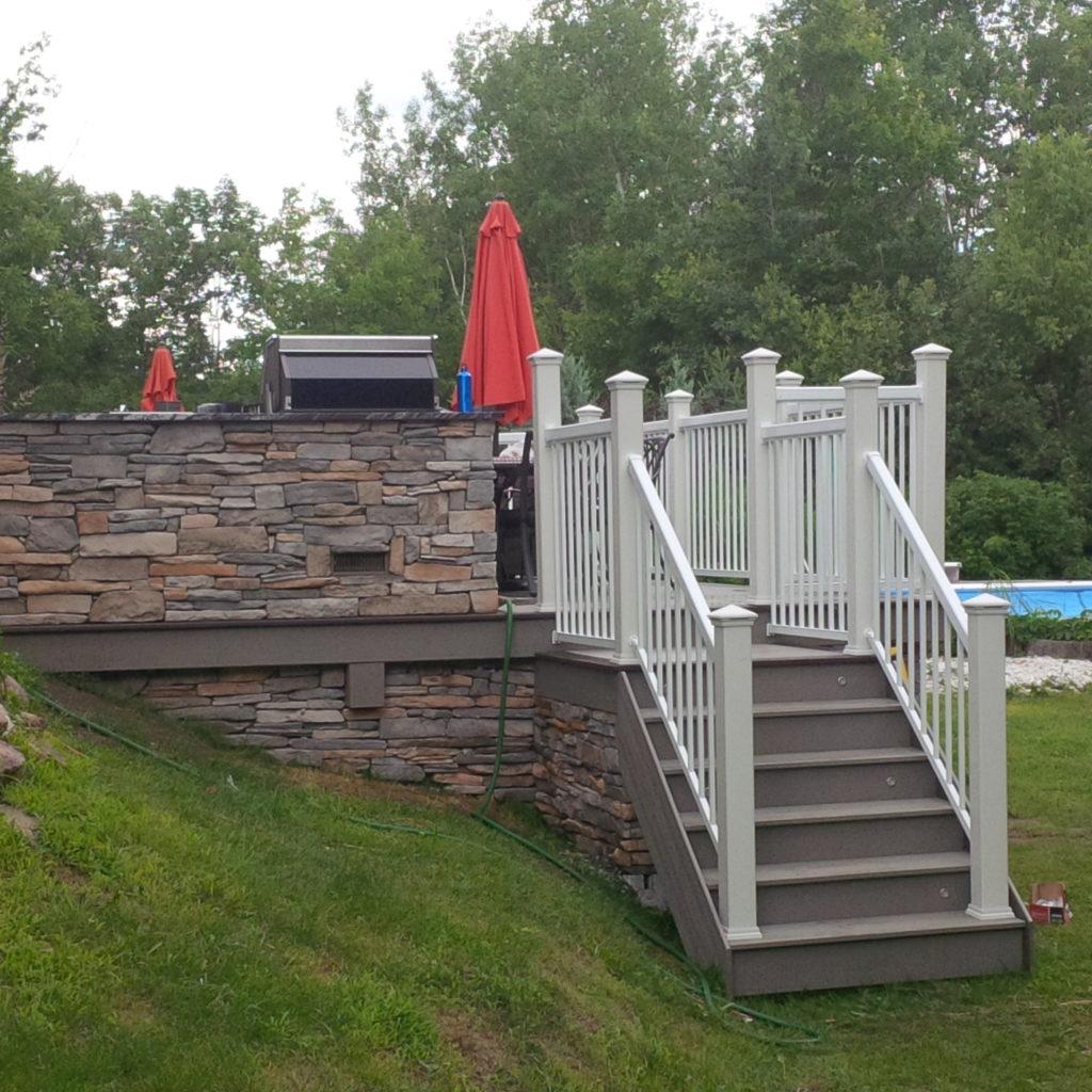 custom deck with stone walls and stairs with railings leading to backyard grass