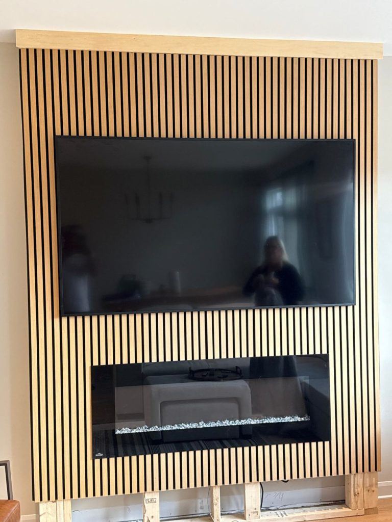 Wall-mounted TV above a modern linear fireplace with vertical wood slat paneling.